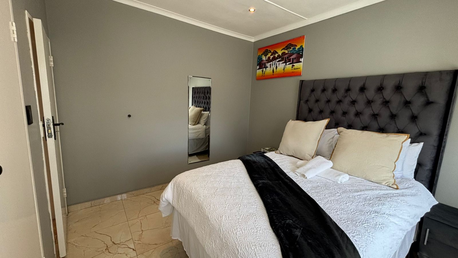 Close bedroom view with tufted headboard and wall mirror
