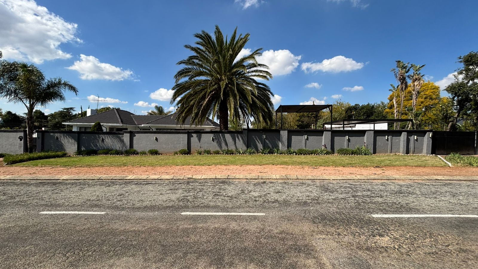 Wide street view of the Bella Vista boundary wall and palms